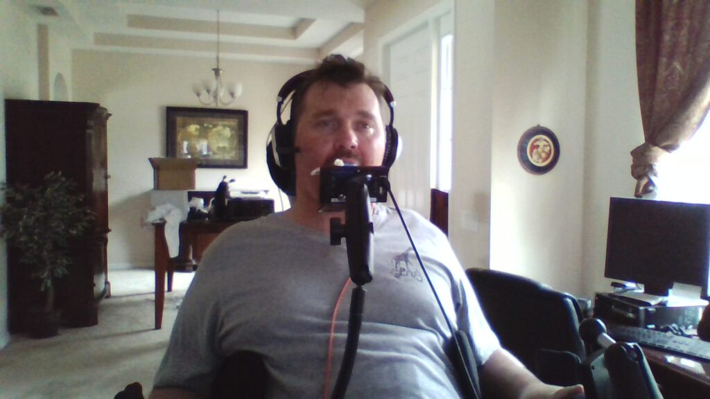 Charlie using a QuadStick mouth controller and headset at his computer.