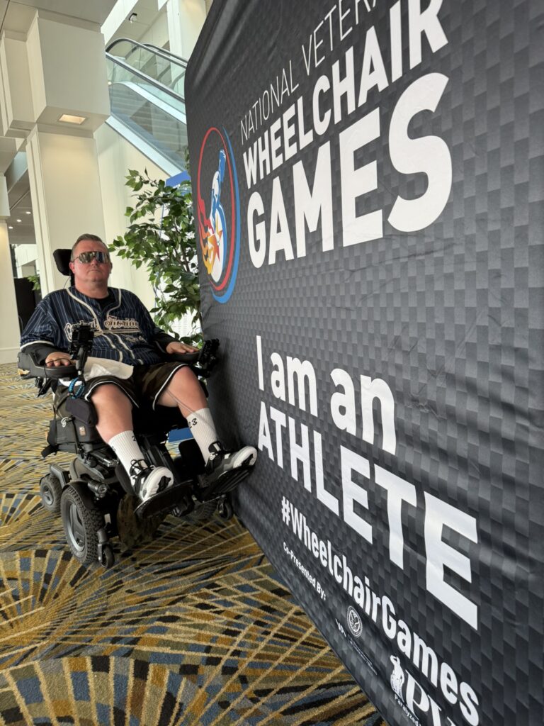 Charlie Merritt of QuadCapable beside the National Veterans Wheelchair Games sign in Detroit.