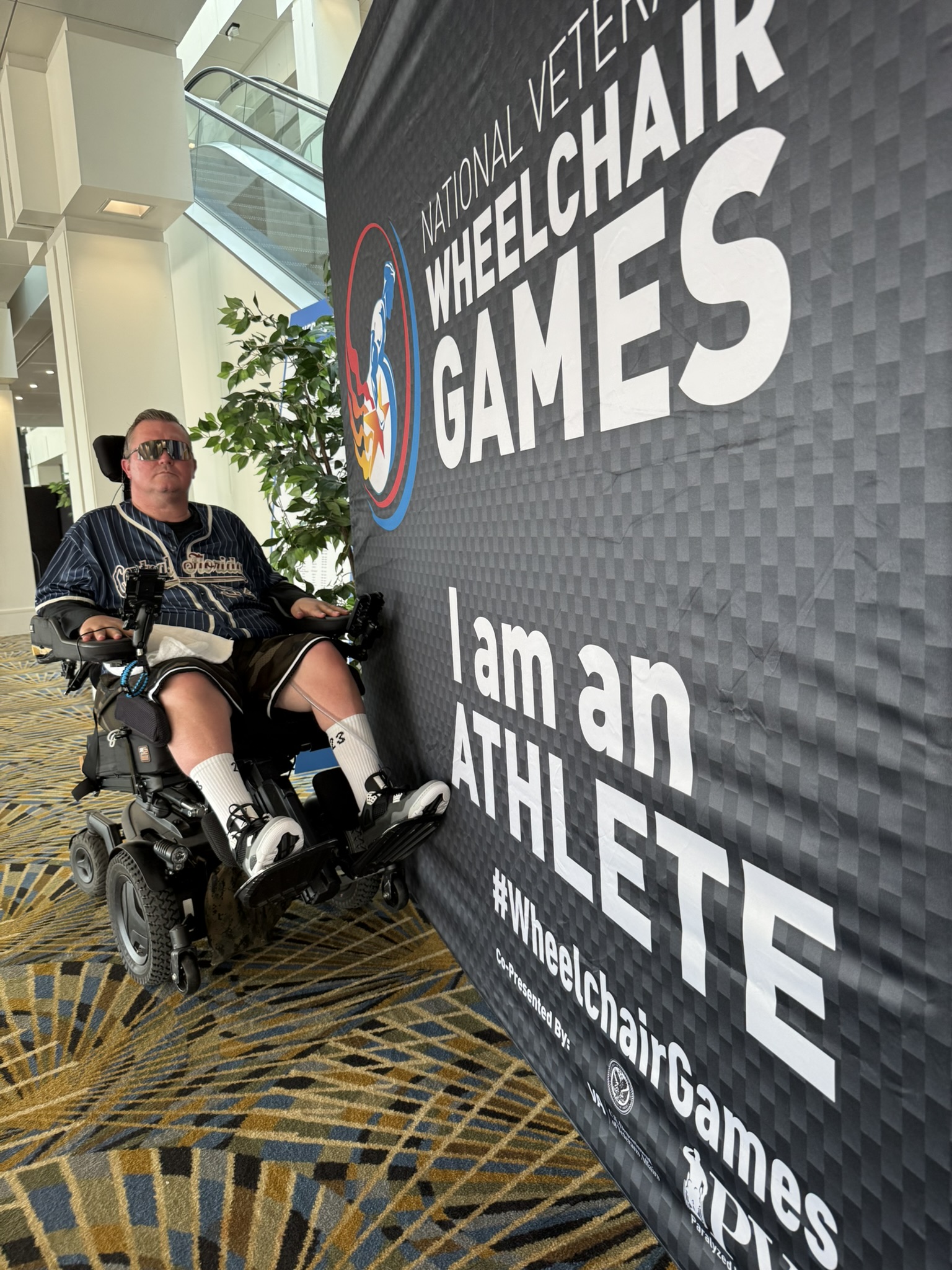 Charlie Merritt of QuadCapable beside the National Veterans Wheelchair Games sign in Detroit.