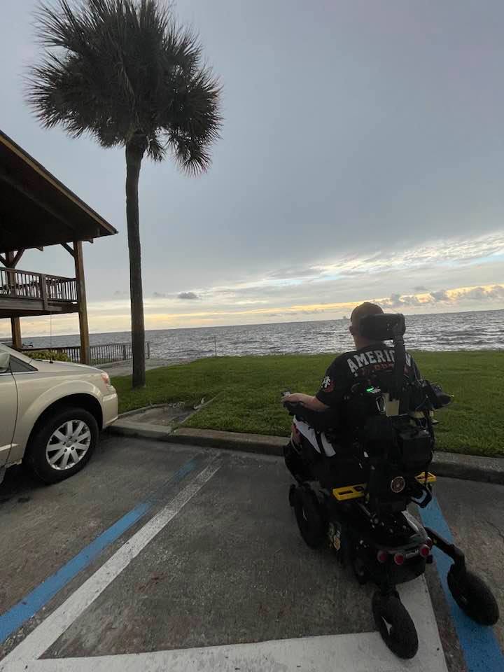 Charlie in his power wheelchair parked near the water at sunset.